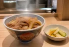 湯気の立つ牛めしとサイドメニューが並ぶ和食チェーン店のカウンター席のイメージ