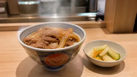 湯気の立つ牛めしとサイドメニューが並ぶ和食チェーン店のカウンター席のイメージ
