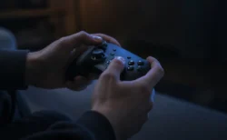 テレビの光を受けてゲームコントローラーを操作する手元