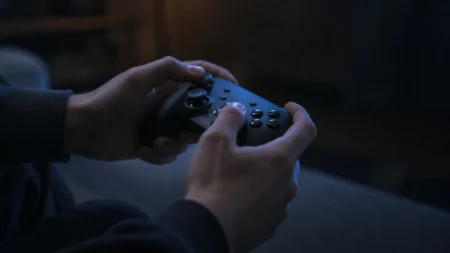 テレビの光を受けてゲームコントローラーを操作する手元