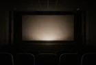無人の映画館スクリーン前、暗闇の中でスクリーンに柔らかい光が投影され始める瞬間の情景