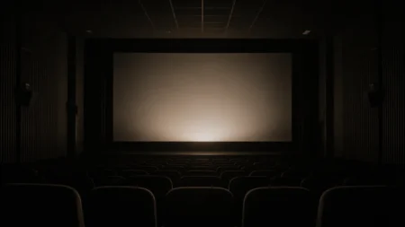 無人の映画館スクリーン前、暗闇の中でスクリーンに柔らかい光が投影され始める瞬間の情景
