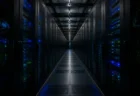 青と緑のインジケーターランプが並ぶ、暗いデータセンターのサーバーラック通路