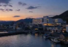 夕暮れ時、海沿いの港町に建つ病院と街並みを望む写実的情景