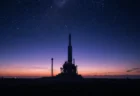 夜明け前の発射場に立つロケットのシルエットと満天の星空、青紫のグラデーション