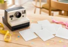 木製テーブルの上にレトロなインスタントカメラと現像したての余白写真、黄色とピンクのリボンや紙吹雪が並んだ写実的な情景