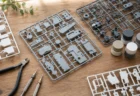木製の作業デスクに並ぶプラモデルのグレーと白のランナー、ニッパーや精密ドライバー、塗料の小瓶を上から撮影したホビー静物写真