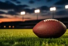 夕暮れのグラウンドに置かれたアメリカンフットボールとぼやけたナイター照明のイメージ