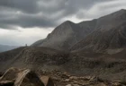 険しい岩山と曇り空、遠くに小さな監視塔のシルエットが見える荒涼とした山岳地帯の情景