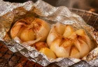 アルミホイルに包んで焼き上げたにんにくが網焼きグリルの上で湯気を立てる写実的な情景