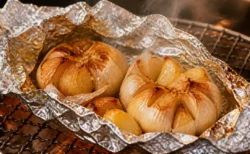 アルミホイルに包んで焼き上げたにんにくが網焼きグリルの上で湯気を立てる写実的な情景