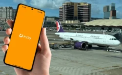 マカオ国際空港の駐機場を背景に、トリファのアプリを起動したスマートフォンを手に持っている様子