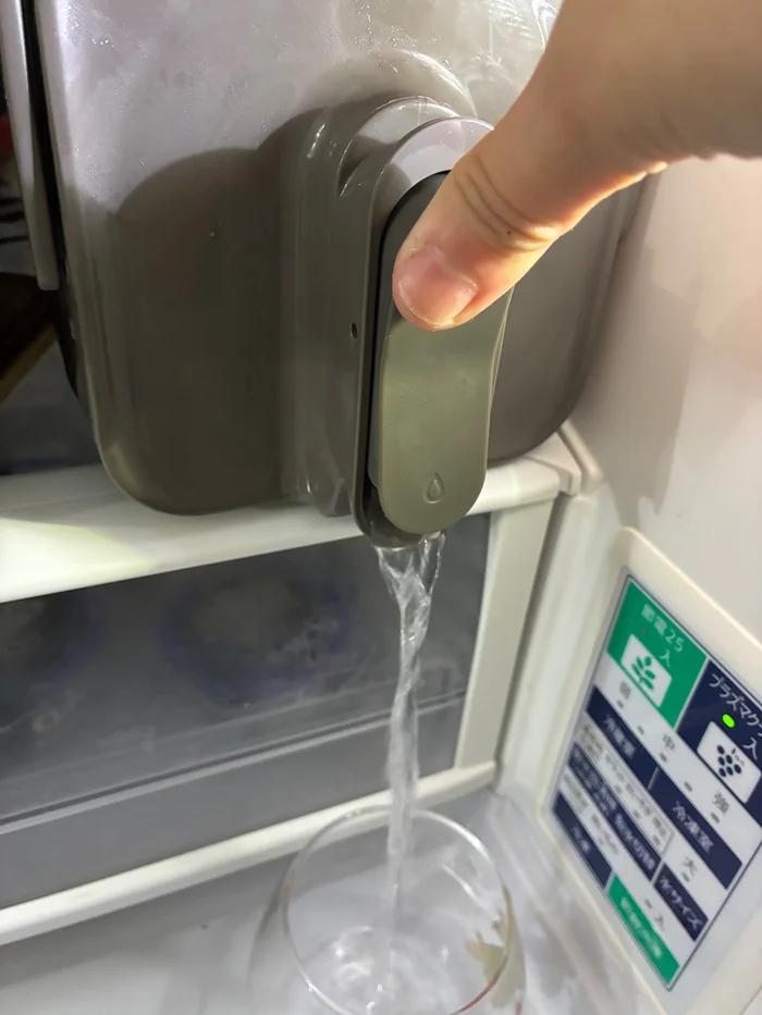 冷蔵庫に入れたスリーコインズ ドリンクサーバーのボタンを押して、グラスに注いでいるところ