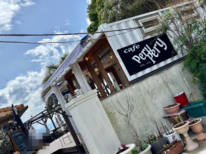 青空の下に立つ cafe perypery の白い店舗と黒い看板、ヤシの木
