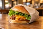 木目のカウンターに置かれた紙包みのチキンチーズバーガー