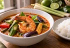 木のテーブルに置かれた赤みがかったエスニックなスープカレーとライス