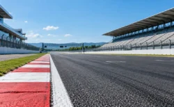 晴れた日の無人のサーキット。ホームストレートのアスファルトと縁石、奥にグランドスタンド