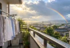 雨上がりの住宅街のベランダに干された洗濯物と、雲間から差す日差しと虹