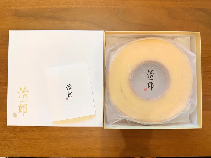 ふたとカードを横に並べた、箱入りの円いバウムクーヘン