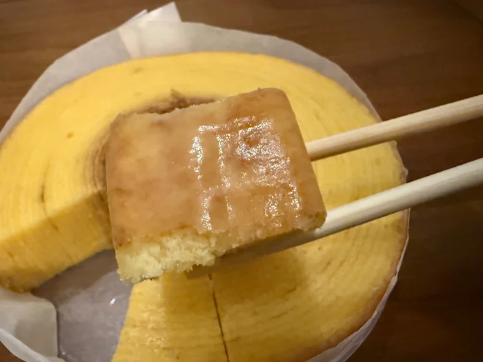外側にお砂糖の衣がついたバウムクーヘンのひと切れをお箸で持ち上げたところ