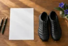 木の机を真上から写した写真。万年筆2本と白い便箋、黒いサッカースパイク、りんどうを生けた花瓶