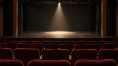 無人の小劇場の舞台を客席側から見た構図。赤い客席の列と、舞台に落ちる1条のスポットライト