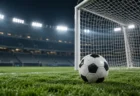 ナイター照明に照らされた無人のサッカースタジアム。ゴール前の芝の上にサッカーボールが置かれている