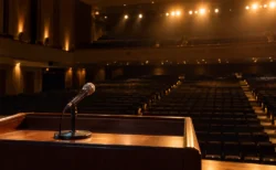 演説会場の演台に置かれたマイクと、客席に向けて照らされたライトの写実的な風景