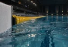 屋内プールのゴール板とレーンロープを水面すれすれから写した写真。水面が波立ち気泡が散っている