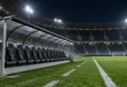 ナイターのサッカースタジアムの控え選手席。屋根付きベンチと照明に照らされたピッチ