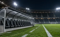 ナイターのサッカースタジアムの控え選手席。屋根付きベンチと照明に照らされたピッチ