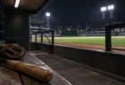 夜の野球場の無人のダッグアウトから見たグラウンドとベンチのバットとグローブ