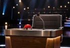 暗いスタジオに照らされたクイズ番組の解答者席。赤い早押しボタンとスタンドマイクが置かれている