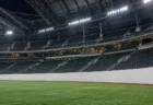 屋内型プロ野球場の右翼スタンドを外野側から見上げた構図。人工芝と白いフェンス、夜間照明