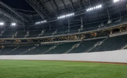 屋内型プロ野球場の右翼スタンドを外野側から見上げた構図。人工芝と白いフェンス、夜間照明