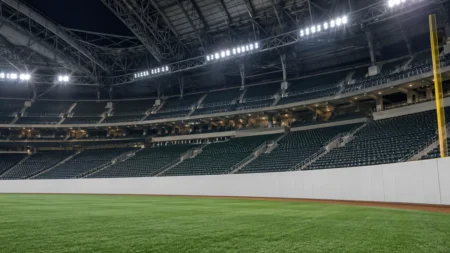 屋内型プロ野球場の右翼スタンドを外野側から見上げた構図。人工芝と白いフェンス、夜間照明
