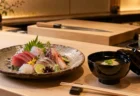和食店のカウンターに並ぶ刺身の盛り合わせと椀物、奥に包丁とまな板