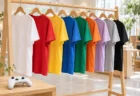 セレクトショップの木製ラックに並ぶ色とりどりの無地Tシャツとゲームコントローラー