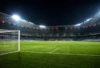 ナイター照明に照らされた無人のサッカースタジアム、芝のピッチとゴールネットのイメージ