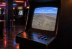 薄暗いゲームセンターのアーケード筐体。画面には荒野の地上絵の上を飛ぶ戦闘機が映っている
