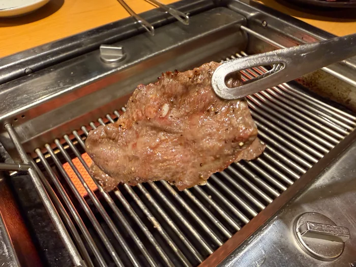 ロースターの網の上でトングに挟まれた焼いたタン