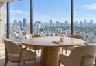 高層階のラウンジに置かれた大きな円卓と椅子、窓の外に昼の東京の街並み
