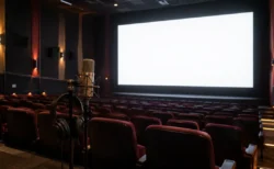 無人の映画館で白く光るスクリーンと、手前に置かれた収録用のスタンドマイクとヘッドホン