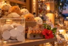 夕暮れの雑貨店の棚に並ぶふわふわのぬいぐるみと、くじ券の入った透明ケース、シーサーの置物と赤いハイビスカス
