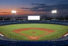 夕暮れの野球場で明るく光る外野の大型ビジョンと青い座席のスタンド