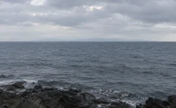 曇り空の下に広がる灰色の海と、水平線にうっすら見える対岸の陸影