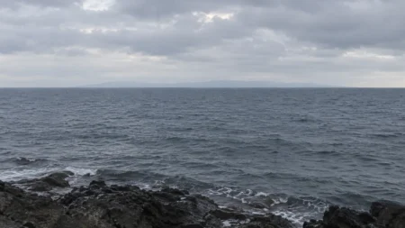 曇り空の下に広がる灰色の海と、水平線にうっすら見える対岸の陸影