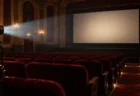 照明が落ちたクラシックな映画館の赤い客席と何も映っていないスクリーン