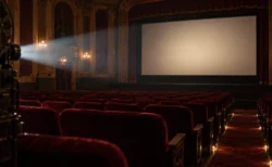 照明が落ちたクラシックな映画館の赤い客席と何も映っていないスクリーン