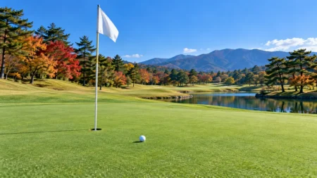 秋の紅葉に囲まれたゴルフ場のグリーンとピンフラッグ、白いボール